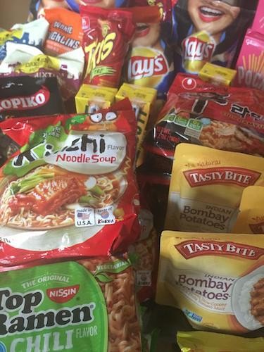 Close-up of food packages including Top Ramen, Kimchi noodle soup, Bombay Potatoes, Lay's chips, takis.