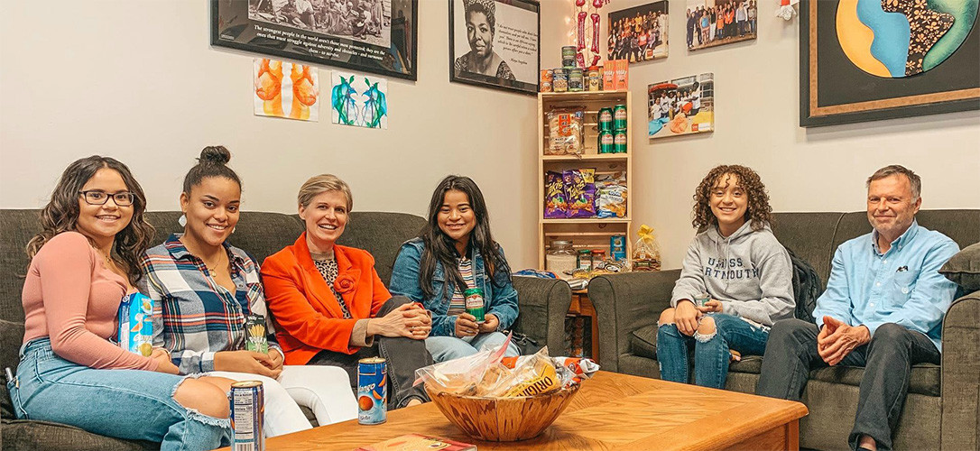 Four female students sitting on couch alongside Rich and Sandra, holding donated goods.